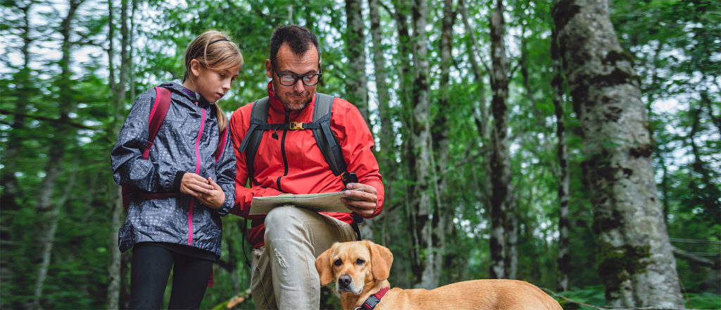 Father and daughter hiking with dog on family camping trip